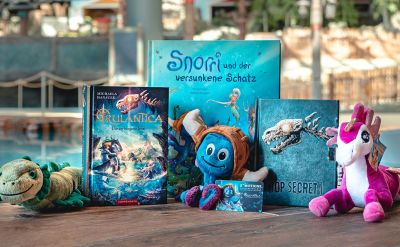 Eine Auswahl aus Produkten von Rulantica: Plüschtiere, Bücher und eine Gutscheinkarte.