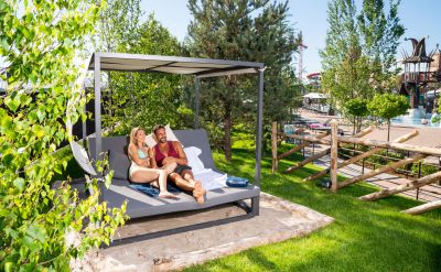 Ein Paar liegt auf einem Strand Sofa im Außenbereich von Rulantica. Im Hintergrund ist die Attraktion Svalgurok zu sehen.