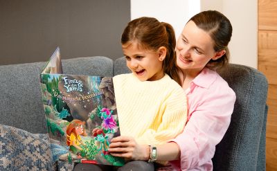 Eine Mutter mit ihrer Tochter liest das Kinderbilderbuch Fina und die Yomis: Das magische Hexenkraut.