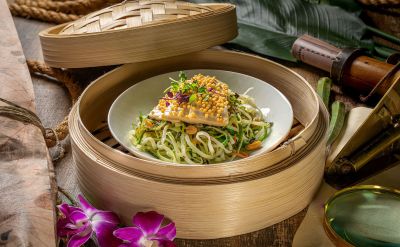 Vegetarische Asia Bowl im Bambuskörbchen mit Tofu, Wakame, Chili, Koriander und Reisperlen. Angerichtet auf einem dunklen Holztisch mit abenteuerlicher Dekoration.