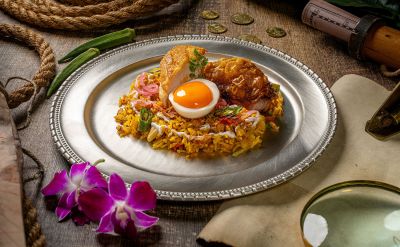 Indisches Biryani mit Reis, Poularde und Ei, serviert auf einem Edelstahlteller mit abenteuerlicher Tischdekoration.
