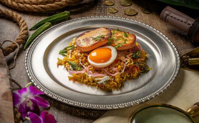 Indisches Biryani mit Reis, Paneer und Ei, serviert auf einem Edelstahlteller mit abenteuerlicher Tischdekoration.