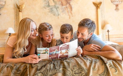Fröhliche Familie auf dem Bett schaut Hotel Plan an