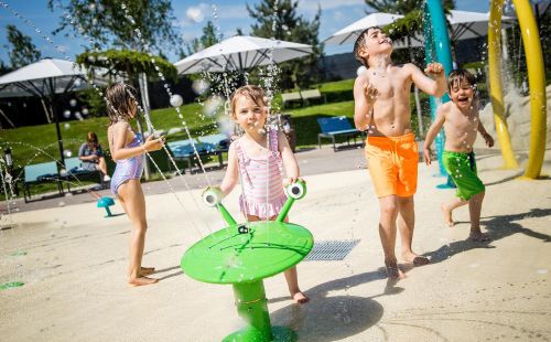 Kinder spielen mit den Fontänen auf dem Wasserspielplatz Snorri Strand