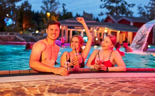 Drei junge Leute am Beckenrand mit je einem Cocktail in der Hand