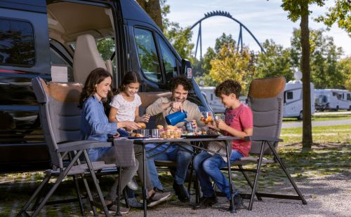 Familie sitzt vor Camper am Tisch beim Frühstück