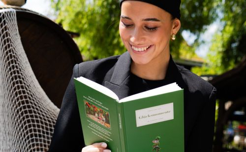 Lächelndes Mädchen schaut sich gerade das Buch "Glücksmomente" an 