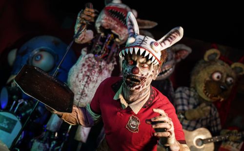 Een Traumatica‑acteur in de gedaante van een zombie, met een griezelige konijnenhoed en een dienblad in de hand. Op de achtergrond zijn andere horrorfiguren te zien.