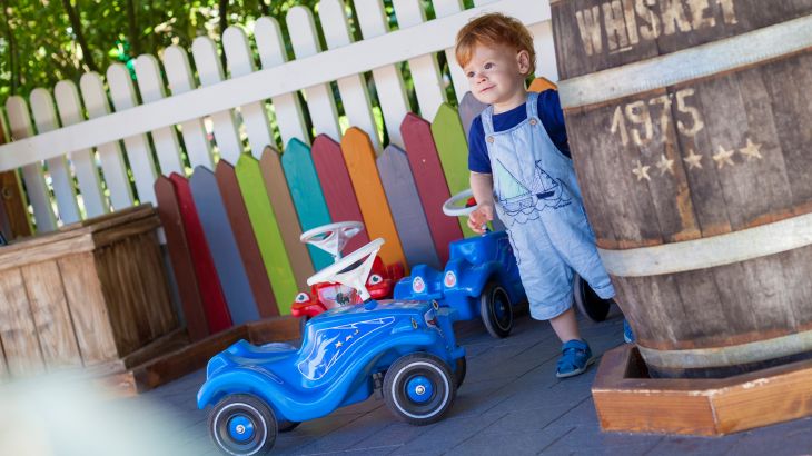 Kind steht neben blauen und roten Bobby-Cars