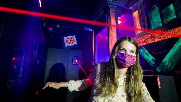 Frau mit Mundschutz läuft durch einen Raum voller Laser