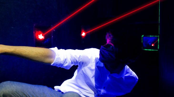 Mann mit Mundschutz krabbelt unter Laser durch