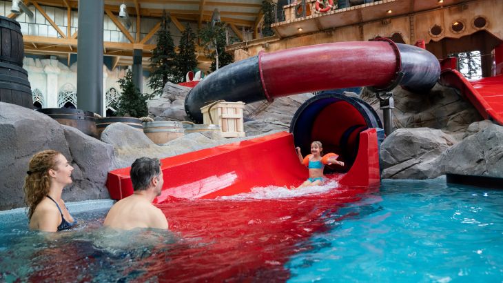 Kind kommt aus der Wasserrutsche "Översnurra", die Eltern warten im Schwimmbecken