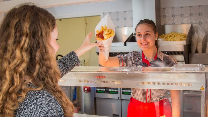 Friethuys Gast erhält eine Tüte Pommesfrites von Angestellter