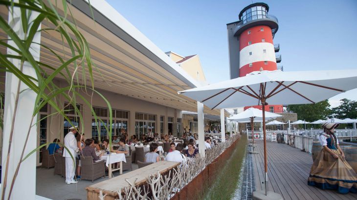 Blick auf die mit Gästen besuchte Terrasse des Harbourside Restaurant und den Leuchtturm
