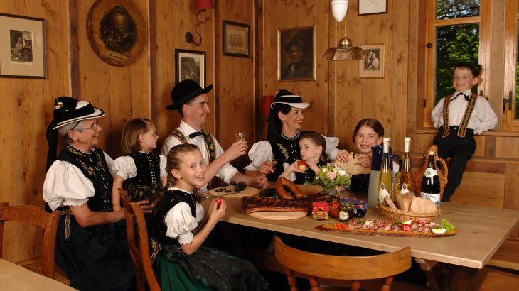Traditionell gekleidete schwarzwälder Familie beim gemeinamen Vesper am gedeckten Tisch