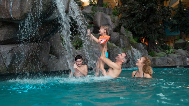 Familie im Wasser in der Skog Lagune, sie stehen unter einem Wasserfall