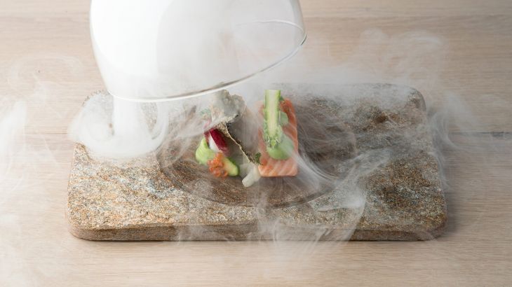 Vorspeise mit Lachs und Gemüse unter einem mit Nebel gefülltem Glas