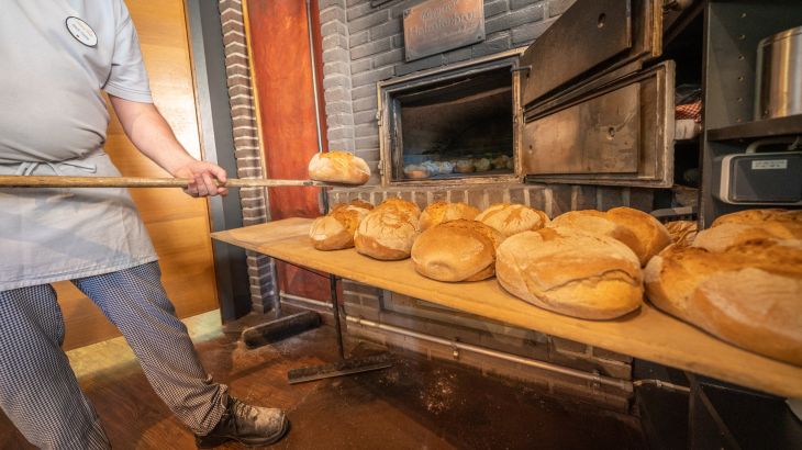 Der Bäcker holt das frisch gebackene Brot aus dem Holzofen