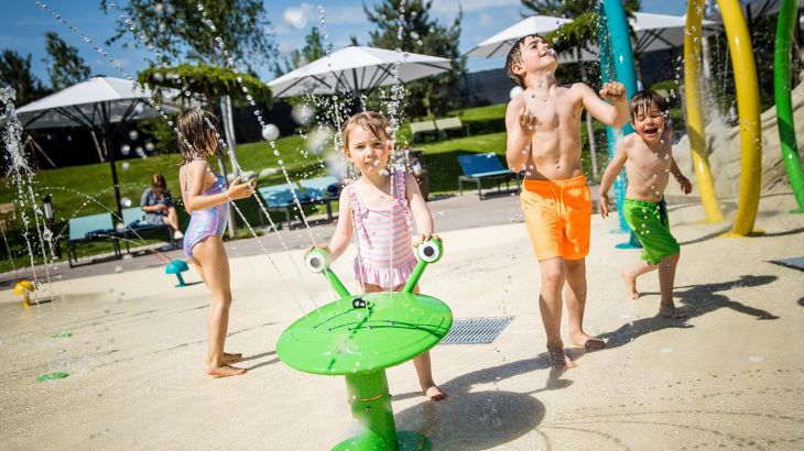 Kinder spielen mit den Fontänen auf dem Wasserspielplatz Snorri Strand