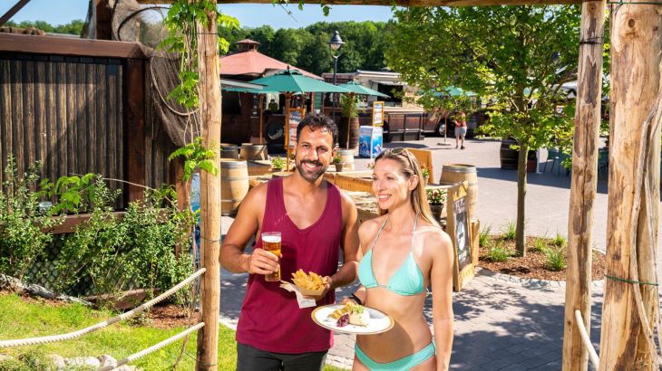 Ein Paar läuft durch den Gastrobereich Strand Kök mit Essen und Getränken in der Hand