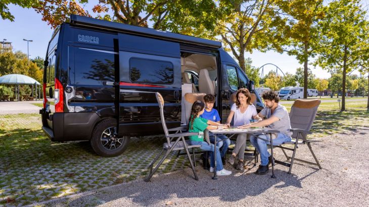 Familie sitzt vor Camper am Tisch