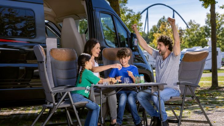 Familie sitzt vor Camper am Tisch Mann jubelt