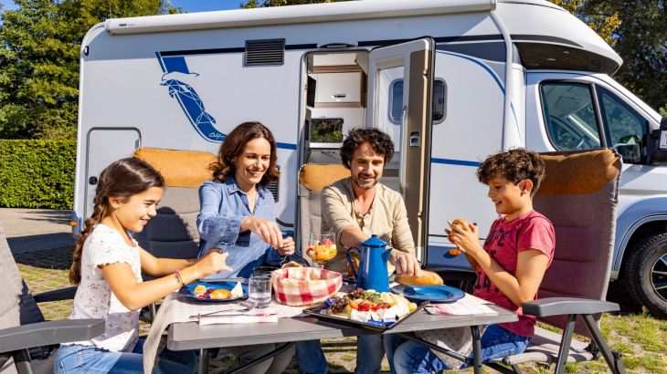 Familie sitzt vor Wohnmobil am Tisch beim Frühstück