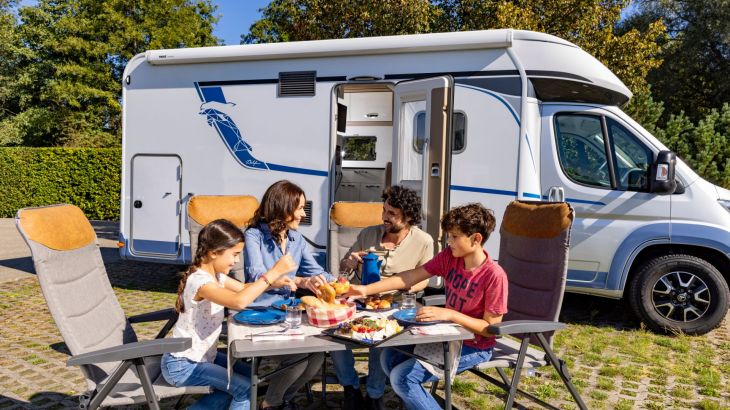 Familie sitzt vor Wohnmobil und frühstückt