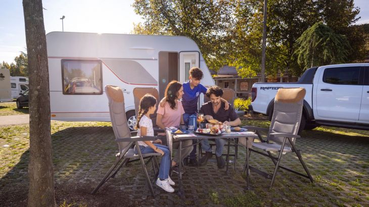 Familie sitzt vor Wohnwagen am Tisch beim Frühstück