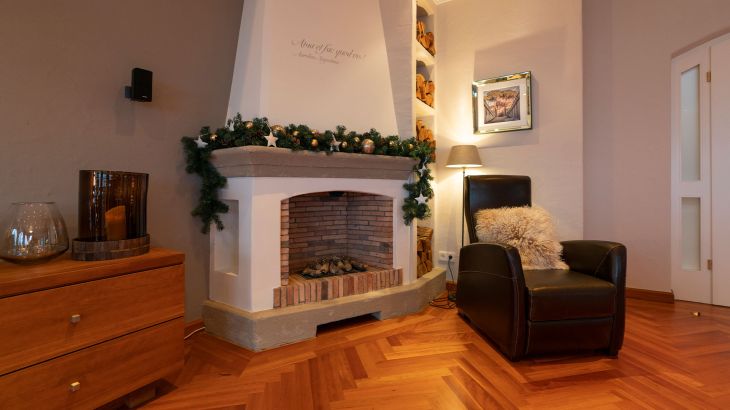 Kamin der vip-Penthouse Suite Rom mit weihnachtlichem Schmuck. Auf der linken Seite eine Holzschränkchen und links ein schwarzer Ledersessel mit Dekokissen