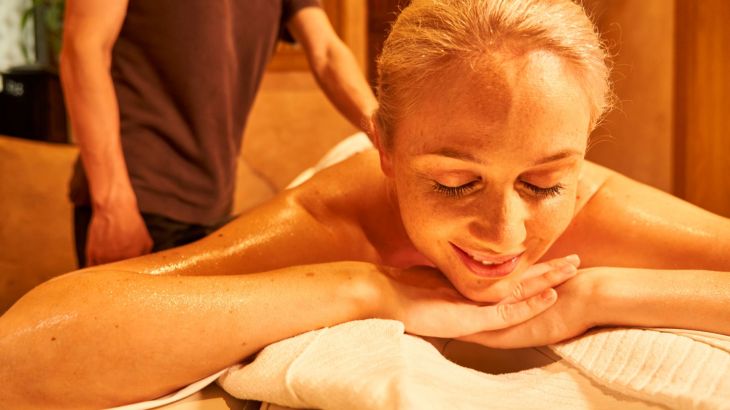 Frau liegt auf Massageliege mit geschlossenen Augen und lächelt