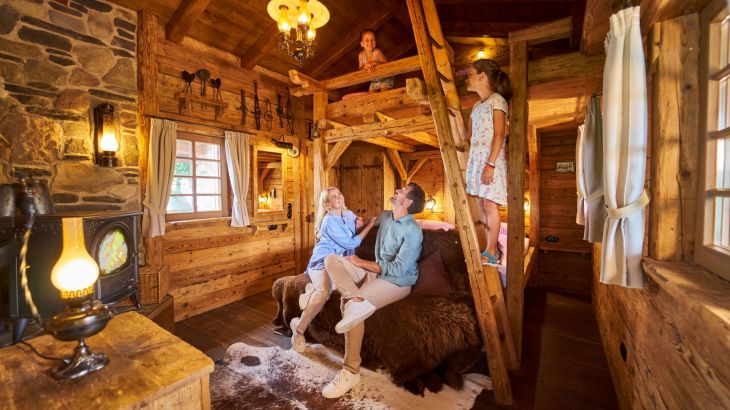 Pärchen sitzt in der Honeymoon Suite auf einer Bank vor dem Bett ein Kind