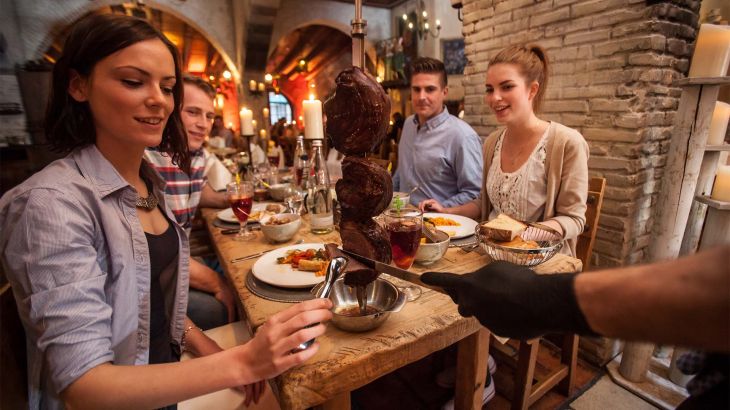 Eine Frau nimmt ein Stück Fleisch von einem klassischen Rodizio Spieß entgegen