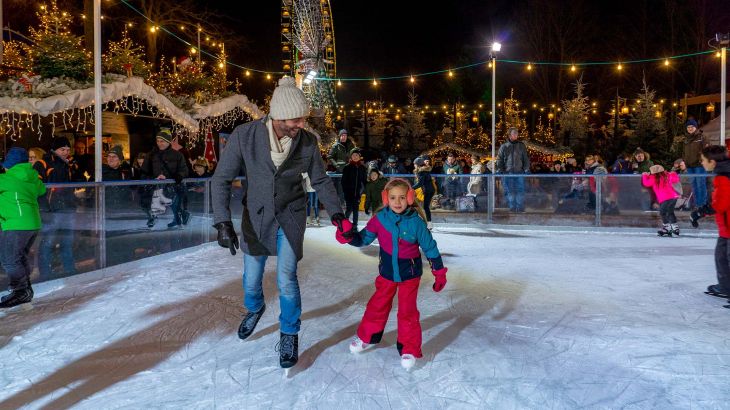 Vater mit kleiner Tochter auf der Eislauffläche