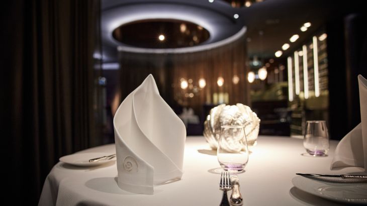 Ein eingedeckter Tisch im Restaurant Ammolite mit einer aufwendig gefalteten Serviette und einer hellen Tischdekoration.