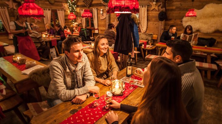 Small groups sit at the wooden tables in the cosy ERDINGER Hütt'n and spend a sociable evening.