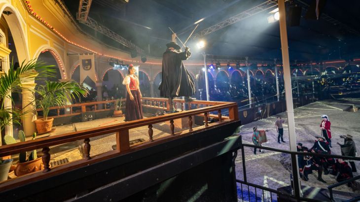 In der Spanischen Arena im Europa-Park steht Zorro auf der Tribüne mit zwei überkreuzten Schwertern. Unten erfolgt ein Kampf.