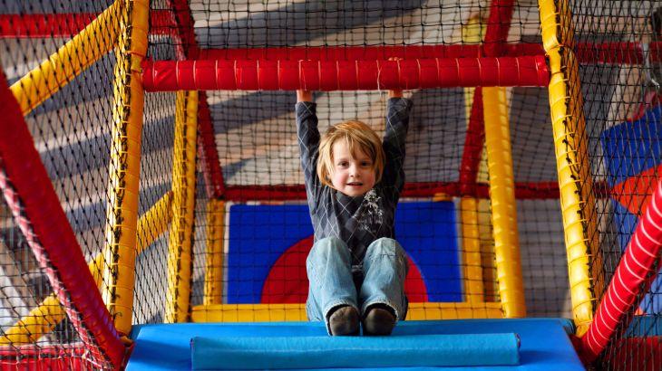 Kind sitzt im Kletterkonstrukt der Casa da Aventura und hält sich an einer Stange über ihm.