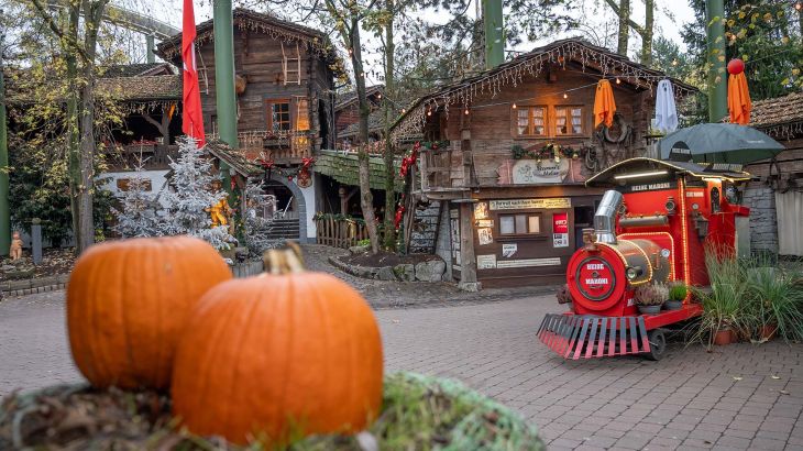 Kürbisse und beschneite Tannenbäume zusammen mit einem Stand für heiße Maronen im Europa-Park.