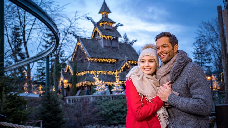 Ein sich umarmendes Pärchen. Im Hintergrund ist die beleuchtete Norwegische Stabkirche zu sehen.