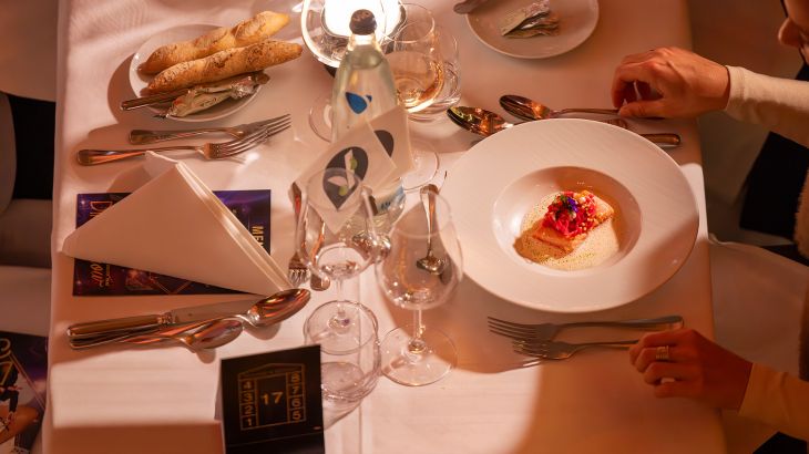 Ein gedeckter Tisch der Dinner-Show. Auf einem Teller ist der erste Gang mit Lachs zu sehen.