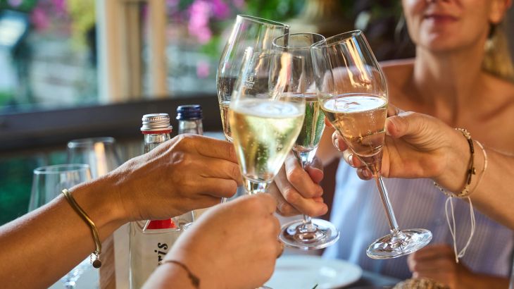 Vier Gäste stoßen mit Weißweingläsern beim Tapas Abend an.