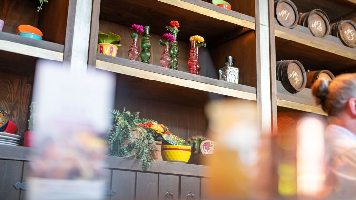 Ein dunkles Holzregal das mit bunten Blumen, Vasen und kleinen Fässern gefüllt ist.