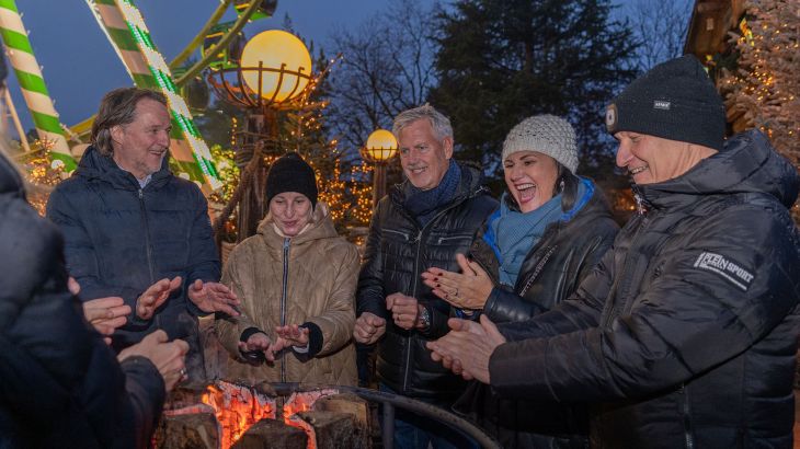 Ein Team steht draußen vor der Erdinger Hütte und wärmt sich die Hände an einem Feuer.