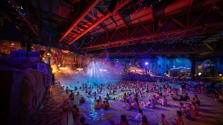 Zuschauer sitzen am beleuchteten Skip Strand in der Wasserwelt Rulantica und bestaunen die Show "NORDLYS – Polar Illumination".