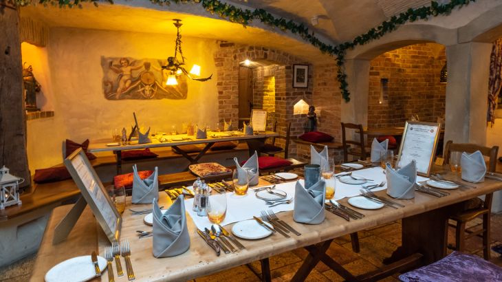 In de Klosterkeller van het 4‑sterren superior themahotel "Santa Isabel" staan feestelijk gedekte tafels; op de voorgrond zijn twee ingelijste awards te zien.