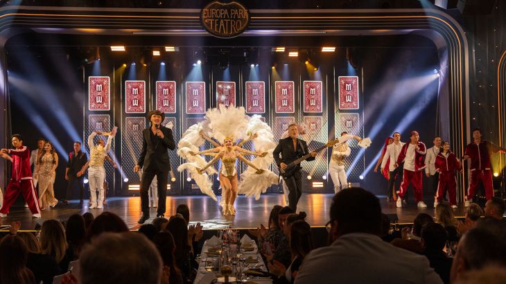 Zwei Musiker performen auf der Bühne im Europa-Park Teatro bei der Dinner-Show. Mit ihnen auf der Bühne sind Tänzerinnen und Tänzer in verschiedenen Kostümen.