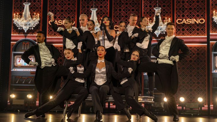 Eine Sängerin und ihre Tanzgruppe performen im schicken Anzug bei der Europa-Park Dinner-Show. Das Bühnenbild stellt ein Casino dar.