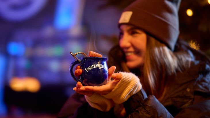 Frau mit Mütze hält eine Feuerzangenbowle in die Kamera