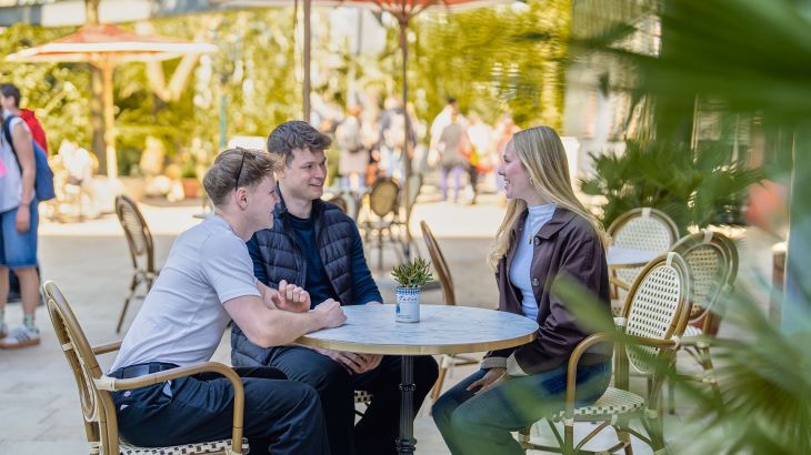 Three people are sitting at a table in the outdoor area of the Monaco themed area at Europa-Park.